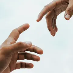 Dwie dłonie wyciągają się ku sobie, symbolizując pomoc i empatię.