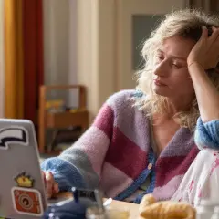 Kobieta z ręką na głowie siedzi przy laptopie, szukając odpowiedzi na pytanie: jak żyć po zdradzie i nie zwariować.