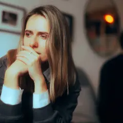 Smutna kobieta zamyślona, z rękami przy twarzy. W tle niewyraźna postać mężczyzny. Obraz symbolizuje obojętność w związku.