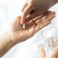 Dłoń podaje kapsułkę, symbolizującą wsparcie dla mózgu po antydepresantach. Obok szklanka wody.
