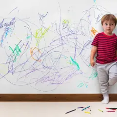 Chłopiec z ADHD, 4-latek, stoi przy ścianie pokrytej kolorowymi bazgrołami. Jego wzrok jest rozbiegany, a postawa sugeruje niepokój.