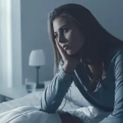 Zmartwiona kobieta w łóżku, zastanawiająca się, co lepsze: estazolam czy nasen. Bezsenność nie daje jej spokoju.