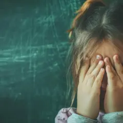 Dziecko z autyzmem zakrywa twarz dłońmi, być może bojąc się hałasu lub nieznanego.