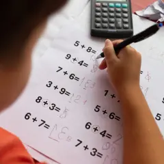 Dziecko zmagające się z zadaniami matematycznymi, co może sugerować dyskalkulię. Widoczne są próby rozwiązań i kalkulator.