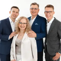 Cztery osoby w eleganckich strojach, uśmiechnięte, na białym tle.