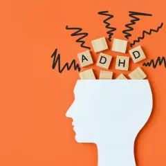 Biały profil głowy z literami "ADHD" na drewnianych kostkach i czarnymi, zygzakowatymi liniami symbolizującymi chaos. Czy ADHD można nabyć?