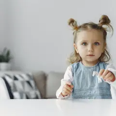 Mała dziewczynka z dwoma kucykami na głowie trzyma w ręku małą figurkę.
