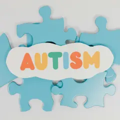 Niebieskie puzzle układanki otaczają chmurkę z napisem AUTYZM. Każdy element to unikalny fragment, jak w spektrum autyzmu i aspergerze.