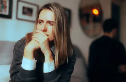 Smutna kobieta zamyślona, z rękami przy twarzy. W tle niewyraźna postać mężczyzny. Obraz symbolizuje obojętność w związku.