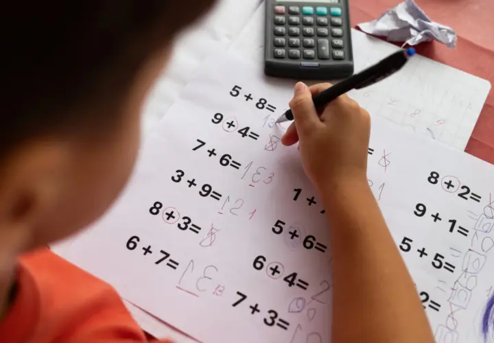 Dziecko zmagające się z zadaniami matematycznymi, co może sugerować dyskalkulię. Widoczne są próby rozwiązań i kalkulator.