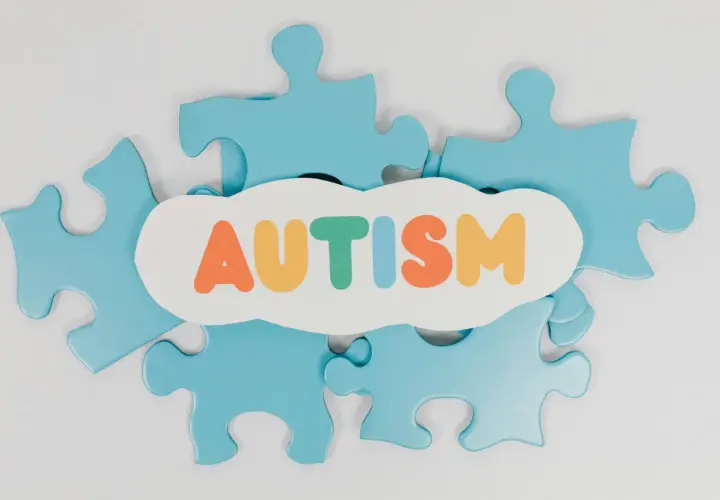 Niebieskie puzzle układanki otaczają chmurkę z napisem AUTYZM. Każdy element to unikalny fragment, jak w spektrum autyzmu i aspergerze.