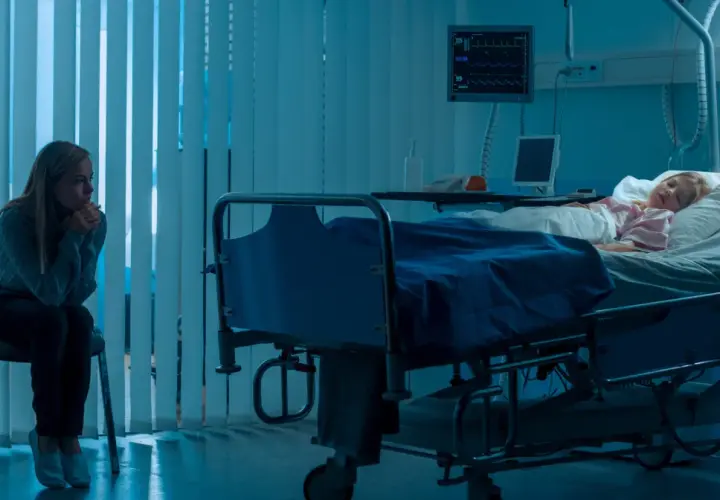 Zmartwiona matka siedzi przy łóżku chorej córki w szpitalu. Scena sugeruje zespół Münchhausena u matek, gdzie matka może wywoływać objawy u dziecka.