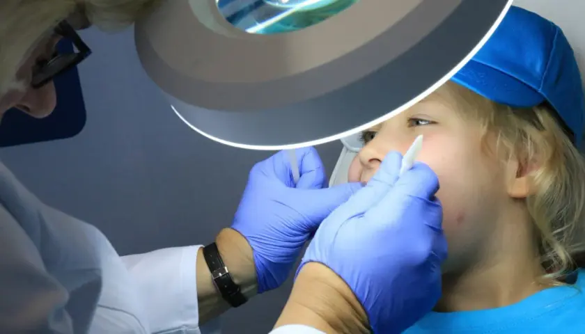 Dentysta w rękawiczkach bada usta dziecka pod lampą powiększającą.