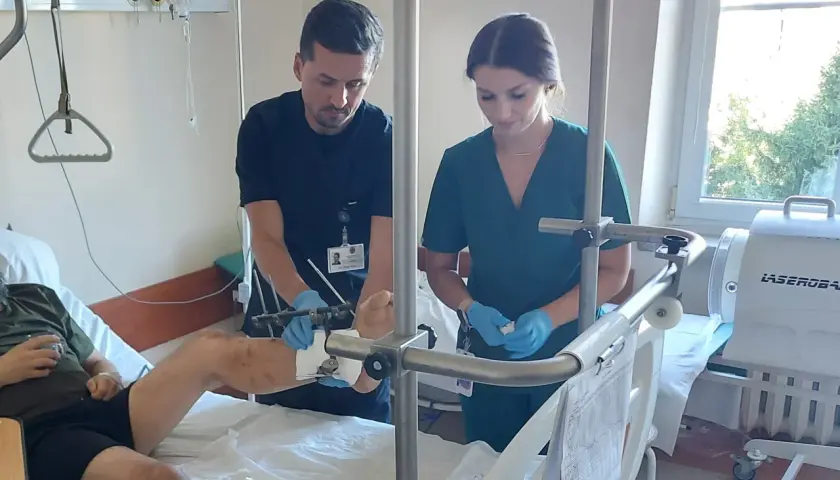Lekarze w szpitalnej sali badają nogę pacjenta z aparatem zewnętrznym.