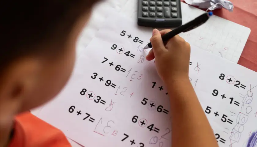 Dziecko zmagające się z zadaniami matematycznymi, co może sugerować dyskalkulię. Widoczne są próby rozwiązań i kalkulator.