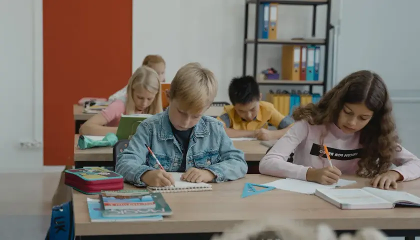Dzieci piszą w zeszytach, ale jedno z nich, z fobią szkolną, czuje się zagubione.