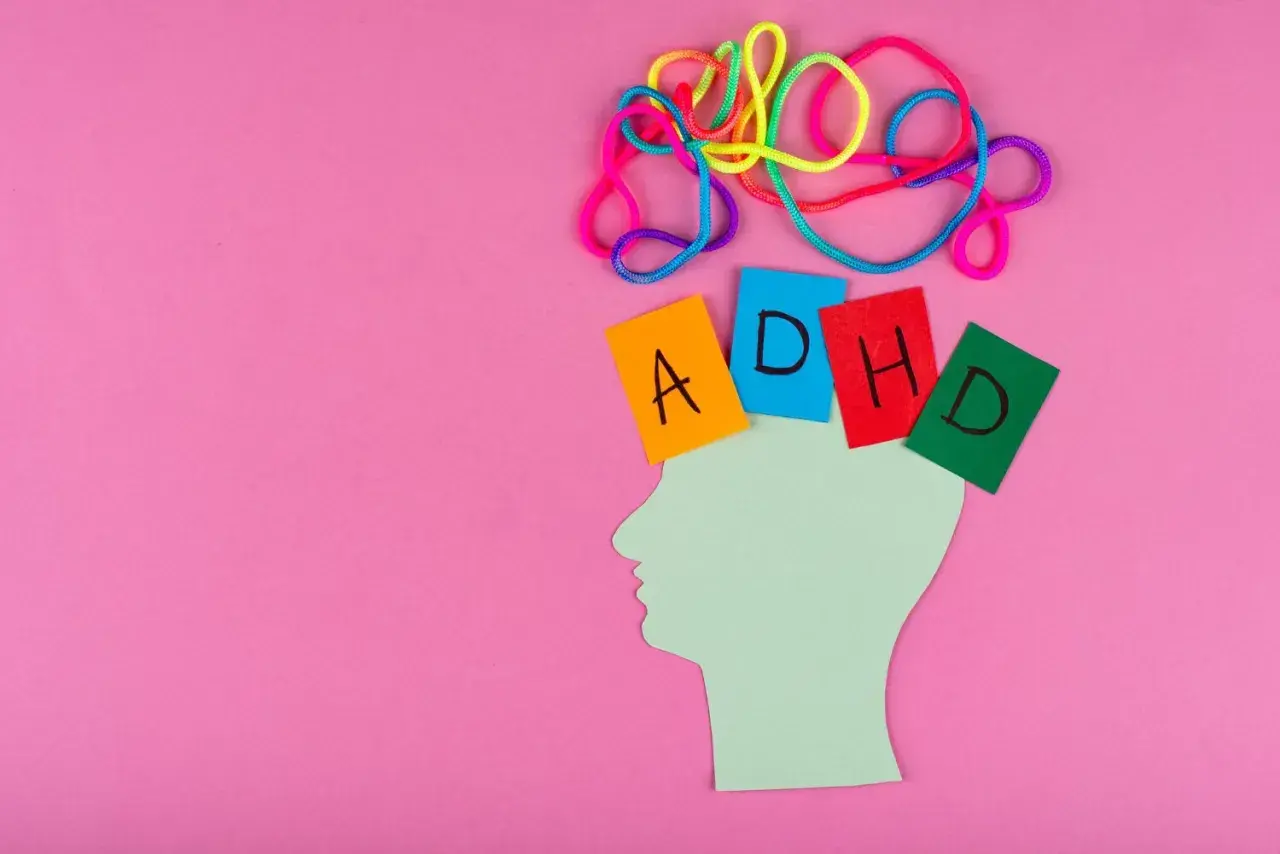 Kolorowe sznurki nad głową symbolizują chaos myśli. Kartki z literami A, D, H, D układają się w napis ADHD.