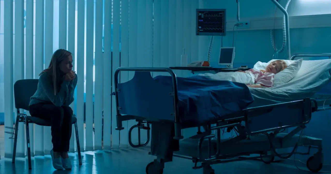 Zmartwiona matka siedzi przy łóżku chorej córki w szpitalu. Scena sugeruje zespół Münchhausena u matek, gdzie matka może wywoływać objawy u dziecka.